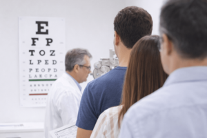 משפחה ממתינה לבדיקת ראייה במרפאת אופטומטריה עם לוח בדיקת עיניים ברקע